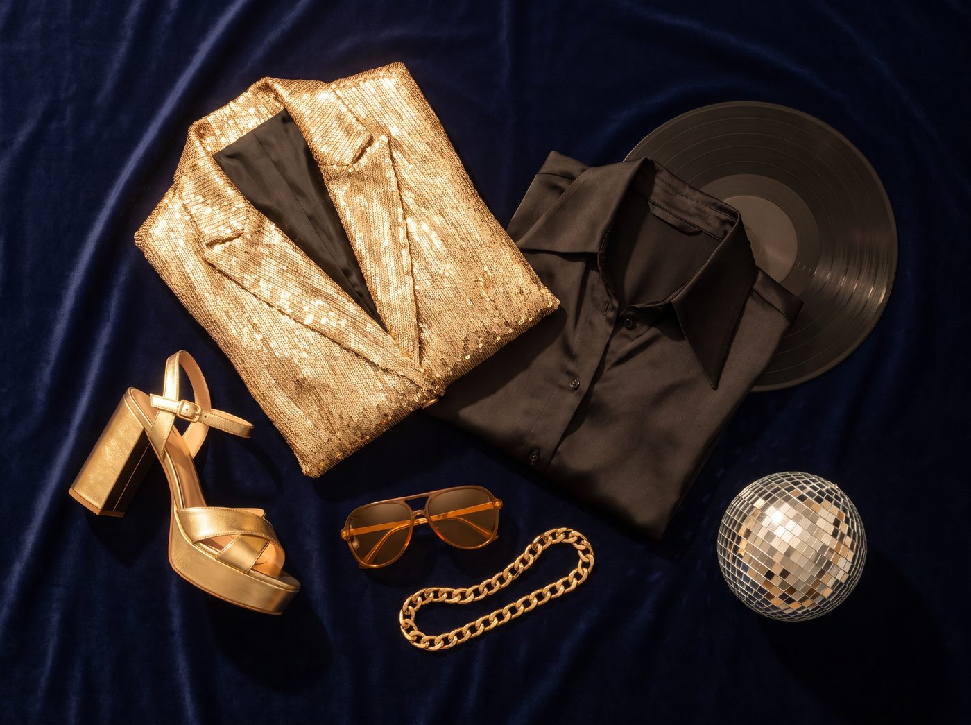 Peças de dress code disco: blazer dourado, camisa de cetim, sapato plataforma, correntes e disco de vinil